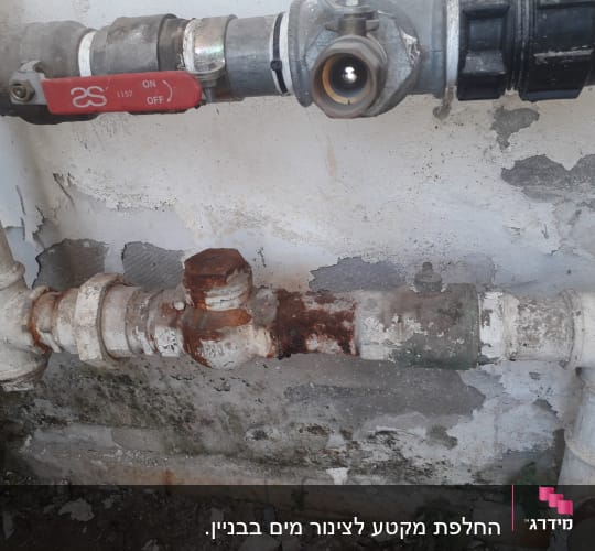 צינור חלוד עם ברז אדום על קיר מתקלף
